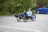 Ein Mann mit Fahrradhelm fährt ein dreirädriges Liegerad auf einem Parplatz.
