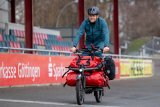 Ein Mann fährt mit einem Lastenrad vor den Zuschauerrängen einer Radrennbahn entlang.