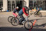 Ein Mann bremst sein E-Bike zwischen orangefarbenen Hütchen. Das Hinterrad hebt dabei vom Boden ab. Im Hintergrund schauen mehrere Personen zu.