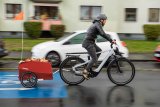 Ein Mann fährt auf einer Fahrradstraße mit einem E-Bike durch ein Wohngebiet. Am Rad hängt ein roter Anhänger.