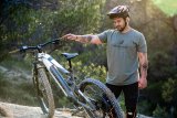 Ein Mann steht in der Natur neben einem E-Bike und betrachtet es.