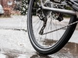 Bild des Hinterrades eines Fahrrades, dass durch eine Pfütze fährt. Vom Reifen spritzt Wasser.