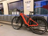 Ein rotes E-Bike lehnt in einem Zug an Klappsitzen.