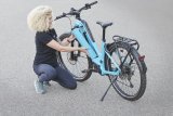 Eine Frau kniet neben einem E-Bike und setzt den Akku in den Rahmen ein.