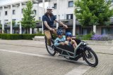 Ein Mann transportiert zwei Kinder in einem Lastenrad.